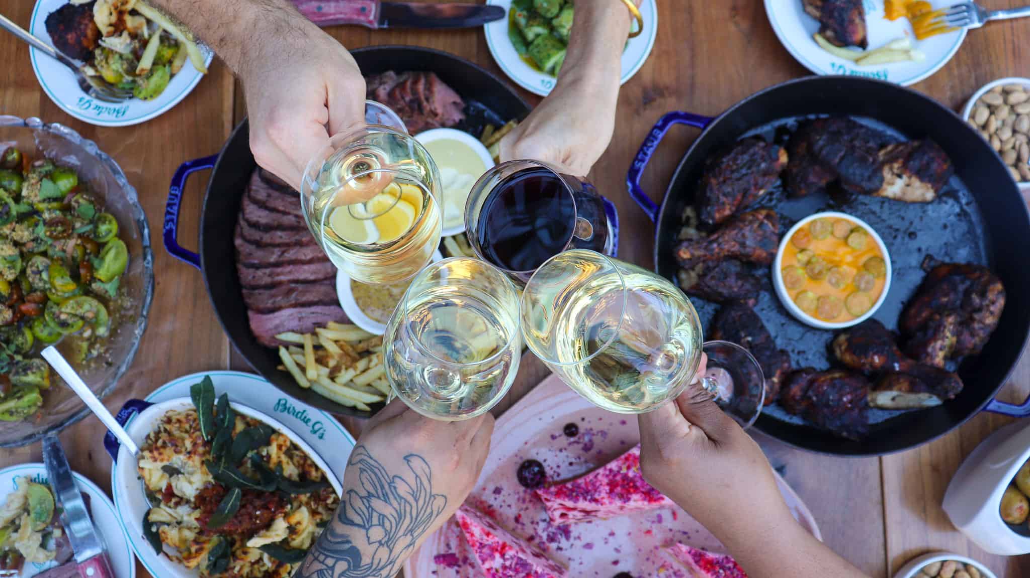 Hands clinking glasses over a variety of dishes