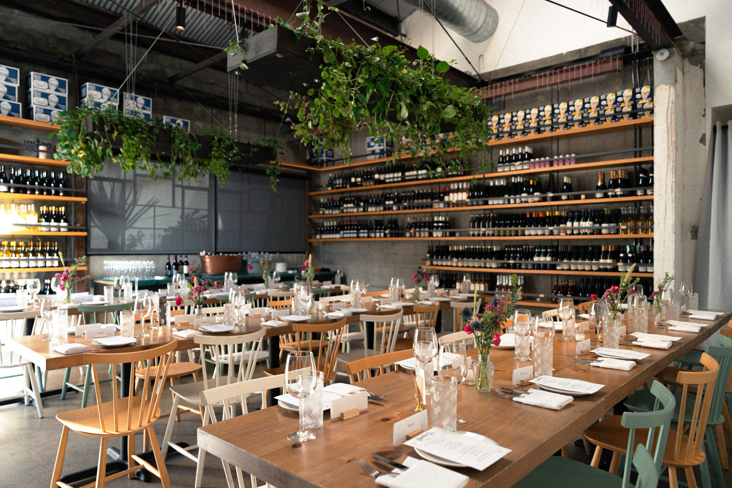beautifully set tables with fresh flowers, green plants hanging from the ceiling and bottles of wine against the wall